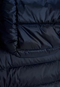 Gros plan d'un tissu matelassé bleu foncé avec des coutures horizontales, montrant la texture et le gonflant d'une veste matelassée.