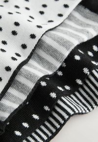 Cztery pary skarpet w kolorach czarnym, szarym i białym. Wzory obejmują kropki, paski oraz różne faktury materiału.