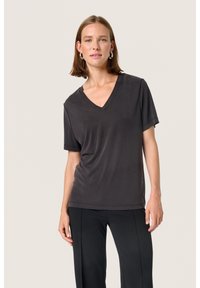 Tricou scurt cu mânecă scurtă de culoare gri închis, cu un design în formă de V. Fabricat dintr-un material neted, are o croială lejeră și este purtat cu pantaloni negri.