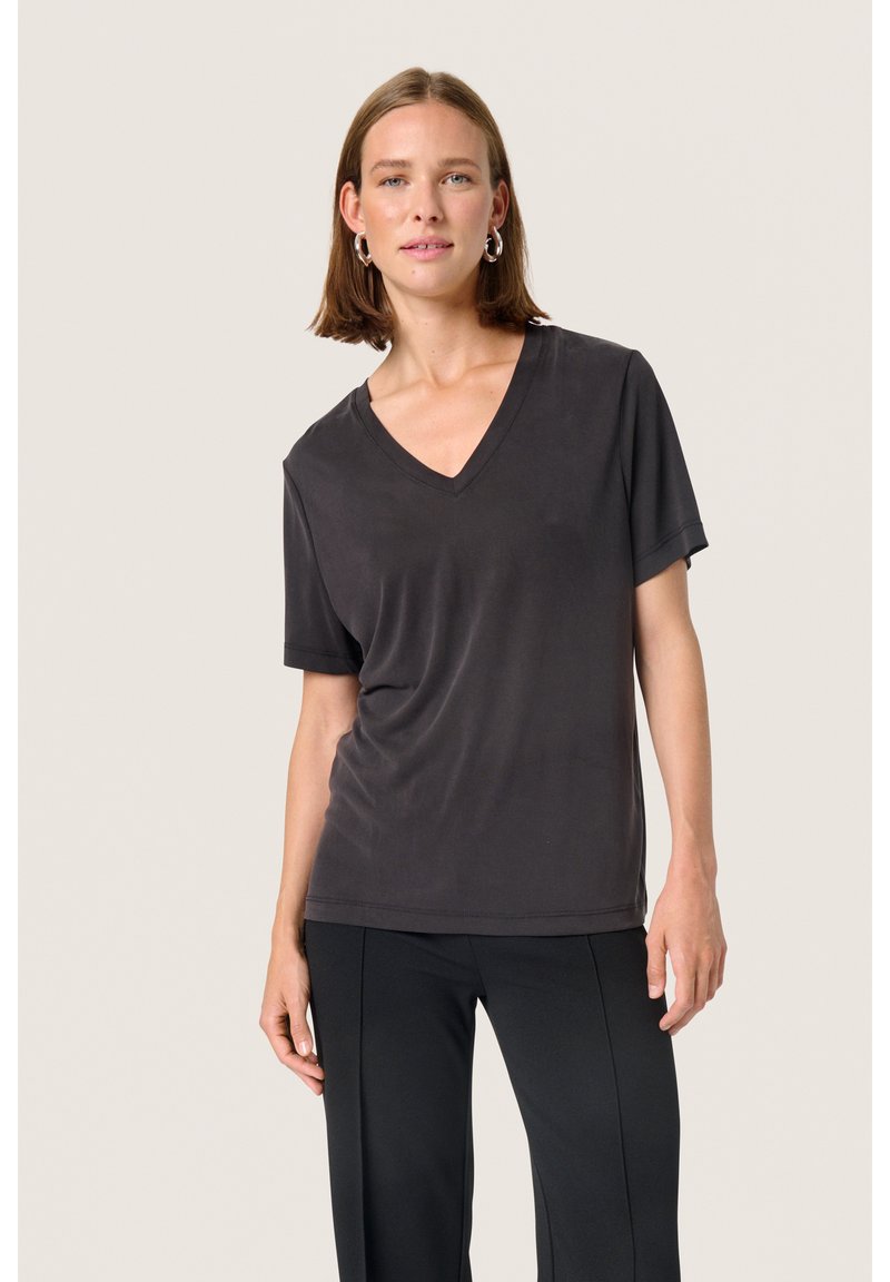Tricou scurt cu mânecă scurtă de culoare gri închis, cu un design în formă de V. Fabricat dintr-un material neted, are o croială lejeră și este purtat cu pantaloni negri.