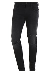 Jeans de mezclilla negra con un corte ajustado, detalles desgastados, parches descoloridos y diseño estándar de cinco bolsillos. Incluyen un cierre de botón.