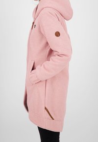 Felpa rosa con zip, dotata di cappuccio, tasche frontali e dettagli in pelle marrone sulle maniche e ai lati, realizzata in tessuto morbido e texturizzato.