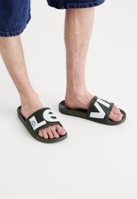 Sandales vertes à glissière avec de grands logos blancs sur les sangles. Matériau en caoutchouc souple, design à bout ouvert et semelle plate.