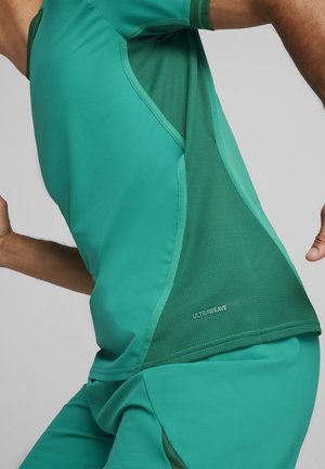 Grünes Sportshirt mit glatter Textur und Netzpaneelen für Belüftung, versehen mit dem Detail "ULTRAWEAVE" an der Seite.