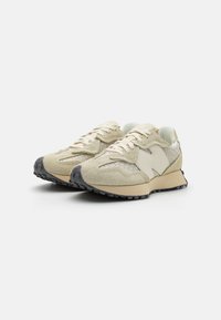 Beige athletic shoes with a textured suede upper, mesh accents, and a black rubber sole. Features a cushioned collar and minimalistic design.