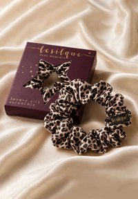 Chouchou en soie de luxe imprimé léopard à côté d'une boîte violette avec une fenêtre en forme d'étoile sur un fond en tissu beige lisse.