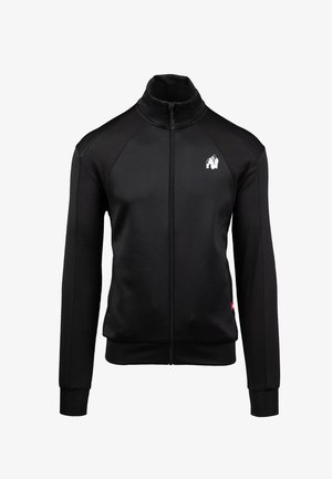Zwarte ritsjack met hoge kraag, textuurpanelen op de mouwen en een wit logo op de borst. Heeft aansluitende manchetten en zoom.