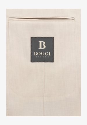 Etichetta rettangolare nera con testo bianco "B Boggi Milano" cucita su una tasca in tessuto beige.
