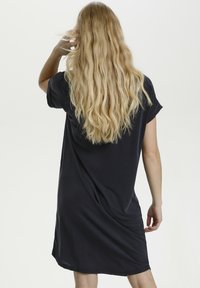 Vestito nero a maniche corte realizzato in un materiale morbido e leggero, con una vestibilità rilassata e una silhouette fluente che arriva sopra il ginocchio.