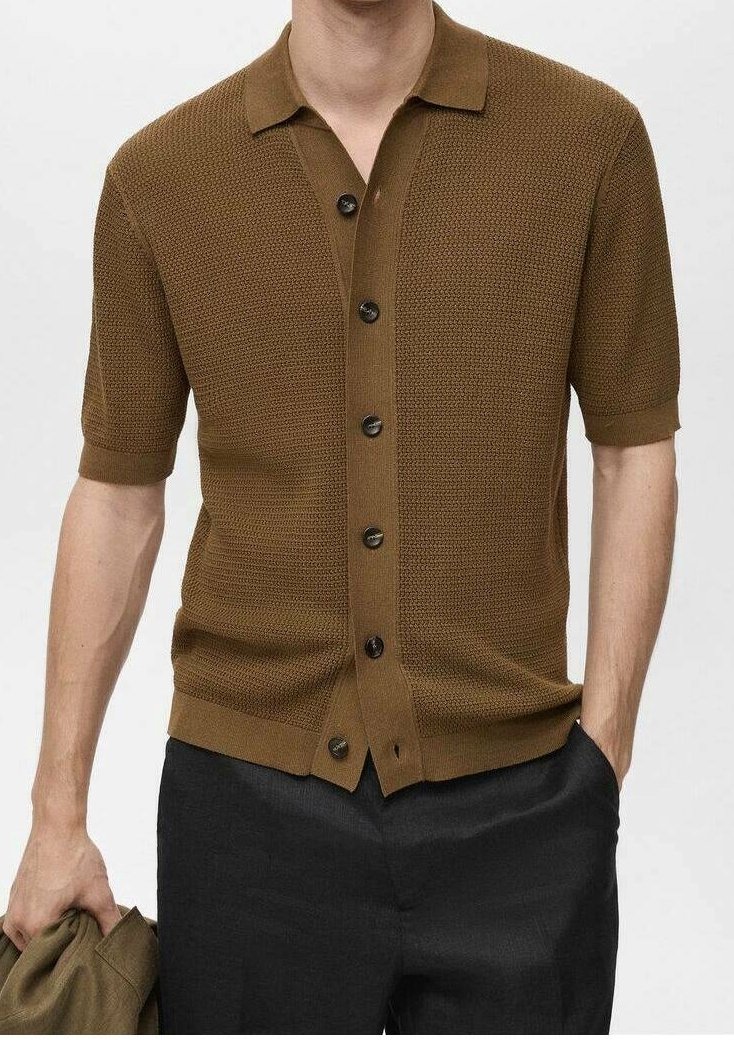 Camisa de punto marrón de manga corta con cuello, presenta un cierre de botones en la parte delantera, tela texturizada y botones oscuros. Llevada con pantalones negros.
