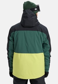 Color-blocked jacket featuring dark blue shoulders, green middle, and bright yellow lower section. Made from textured, water-resistant material.