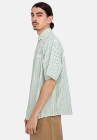 Korte mouwen overhemd in groen en witte strepen met een button-down kraag en een borstzak aan de linkerkant. Gemaakt van lichtgewicht, ademende stof.