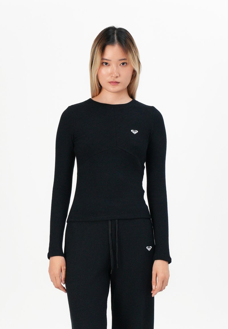 Black ribbed long-sleeve top with a round neckline and a small white heart logo on the chest. Material appears soft and textured.