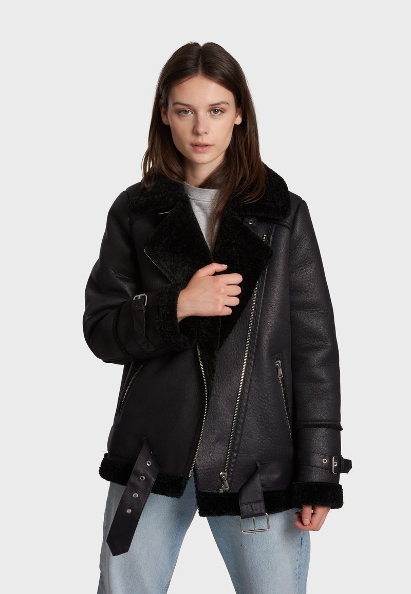 Black leather jacket with a soft black shearling collar, zip closure, and adjustable straps on cuffs and hem. Textured finish, casual design.