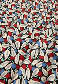 Bavlněná tkanina s černým pozadím, na kterém je vzor červeného a modrého ovoce obklopeného krémovými a světlými zelenými listy.