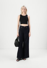 Čierny cropped top s tenkými ramienkami, tmavomodré široké džínsy s vysokým pásom a detailom šitia, doplnené o malú čiernu kabelku a čierne sandále na otvorenú špičku.