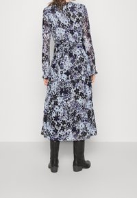 Długa, zwiewna sukienka w jasnoniebieskim kolorze z ciemnymi, kwiecistymi wzorami. Posiada długie rękawy, pasek w talii oraz falbaniaste spódnice. Czarne botki dopełniają stylizację.