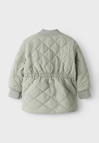 Veste matelassée vert clair avec un motif en losange, taille élastique et poignets côtelés gris. Texture douce et coupe décontractée.