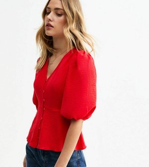 Red puff-sleeve blouse with a deep V-neck, textured fabric, front button closure, and a fitted waist, paired with blue denim jeans.