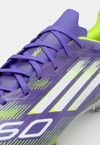 Crampon de fotbal violet cu accente verzi, superior texturat și design cu dungi albe. Dispune de un guler căptușit și sistem de închidere cu șireturi standard.