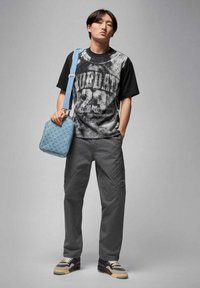 Czarny i szary t-shirt z nadrukiem „JORDAN 23”, szare spodnie typu cargo oraz niebieska torebka na ramię z wzorem. Buty sportowe z czarnymi i kremowymi akcentami.