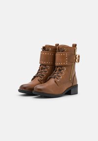 Stivali ankle in pelle marrone con punta rotonda, lacci, cerniera laterale, decorazioni a stud e tacco a blocco basso. Presenta una cintura decorativa.