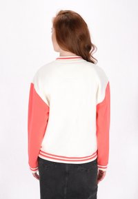 Bluza color-block z białym korpusem, koralowymi rękawami i paskowanymi mankietami. Gładki materiał, luźny krój i okrągły dekolt.