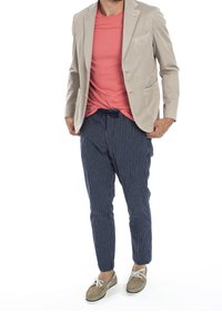 Ljus beige blazer över en korallfärgad t-shirt, ihop med marinblå byxor med ränder och bruna skor. Outfiten har avslappnade, lediga inslag.