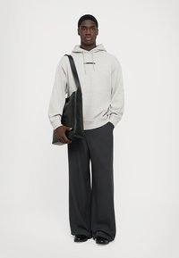 Hanorac gri deschis cu logo negru, pantaloni negri oversized, tăiați cu atenție, și o geantă de umăr din piele neagră. Texturi netede și design minimal.