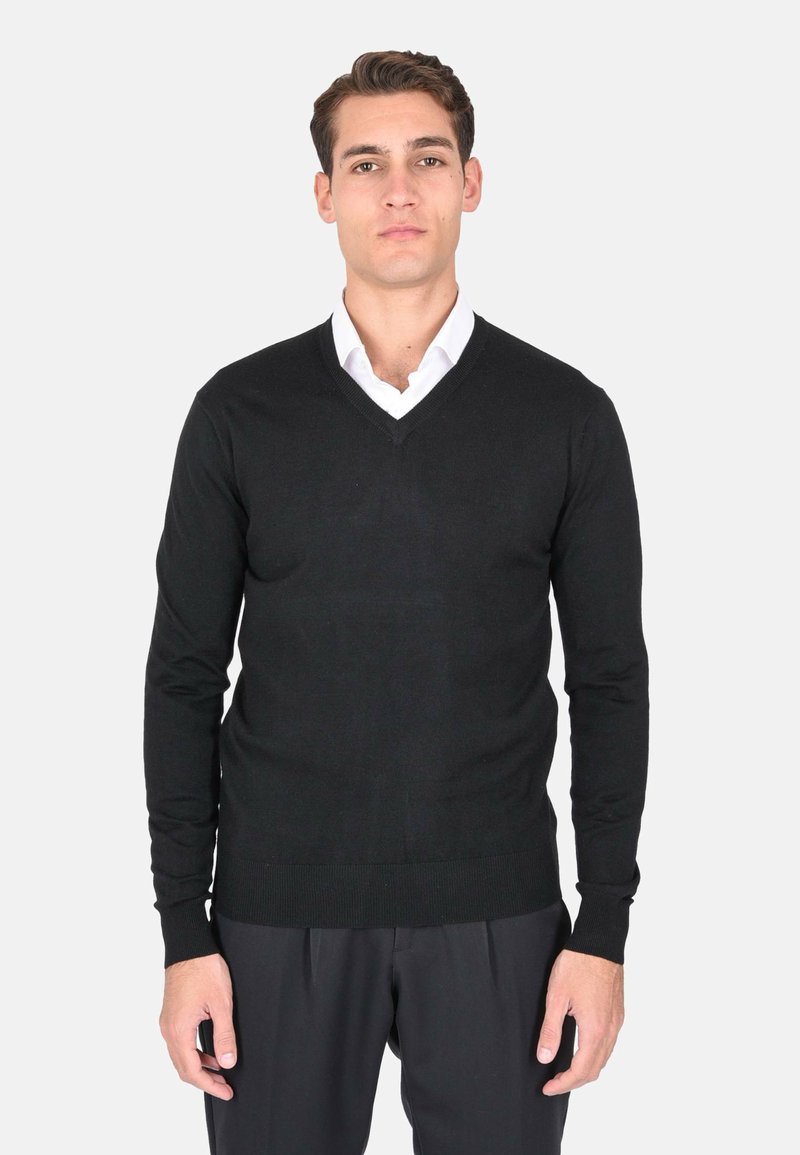 Maglione nero leggero con scollo a V e maniche lunghe. Tessuto lavorato a maglia, silhouette aderente, indossato sopra una camicia bianca.