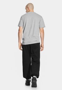 Szara koszulka z krótkim rękawem, luźny krój, zestawiona z luźnymi czarnymi spodniami i czarnymi trampkami. Widoczne detale przeszycia na koszulce i spodniach.