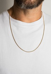 Colier de aur cu un design împletit, așezat pe un tricou alb, evidențiind o finisare netedă și o calitate reflectantă.