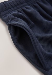 Približen posnetek mornarsko modrega teksturiranega blaga z elastičnim pasom in odprtino stranskega žepa na belem ozadju.