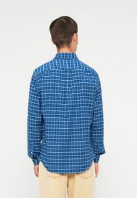 Camisa de cuadros azul con botones, de manga larga, que cuenta con un cuello clásico y un dobladillo curvado. Tejido de algodón ligero con un patrón a cuadros.