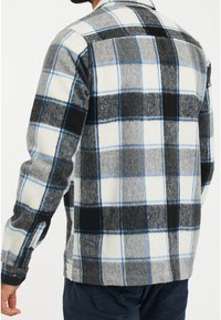 Camicia in flanella a quadri grigia, nera e bianca, con accenti blu. Texture morbida con polsini e colletto a bottoni, dettagli di cucitura visibili.