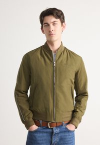 Olive green bomber jacket with zipper closure, elastic cuffs, side pockets, and white stripe accents on sleeves; lightweight fabric.