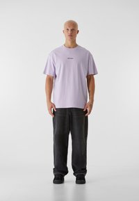 Lilla bomull T-skjorte med rund hals og korte ermer, med teksten "LOST YOUTH" i svart. Brukt med svarte løstsittende jeans og joggesko.