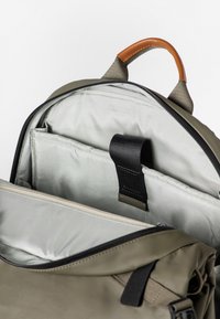 Zaino verde oliva con chiusura con zip, maniglia superiore in pelle e più scomparti con fodera grigia liscia e spallacci neri.