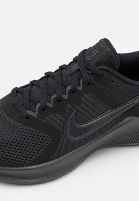 Zapatilla deportiva negra de Nike que presenta materiales de malla y sintéticos, patrones texturizados y un logotipo tonal. Diseño con cordones y suela duradera.