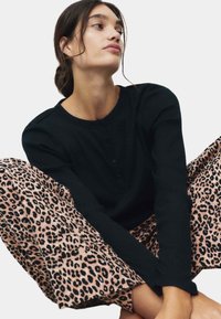 Sort ribbet langærmet top med rund halsudskæring, parret med pink leopardmønstrede brede bukser med en blød tekstur.