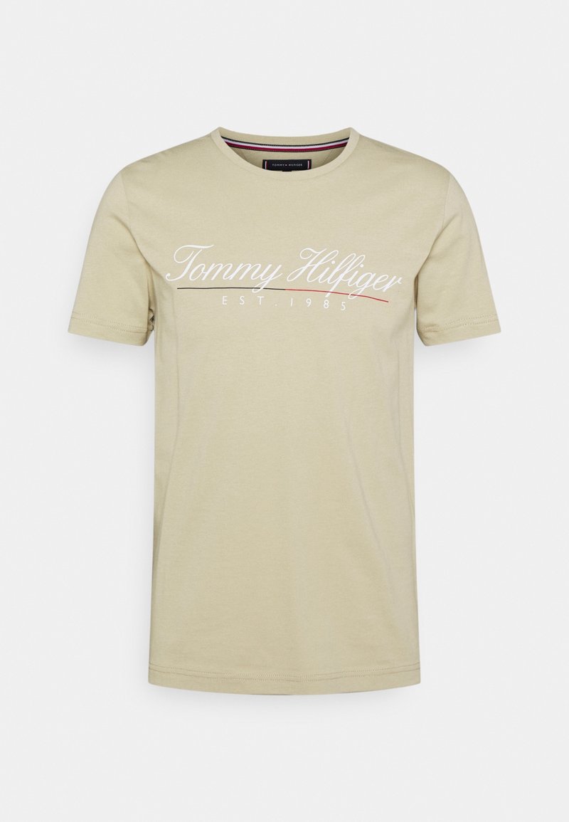 Beżowy bawełniany t-shirt z krótkimi rękawami, okrągłym dekoltem i białym logo „Tommy Hilfiger EST 1985” na przodzie.