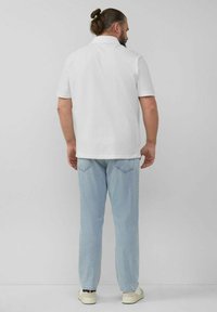 Weißes Poloshirt mit kurzen Ärmeln, kombiniert mit hellblauen Jeans und weißen Sneakers, zeigt eine lockere Passform und simples Design.