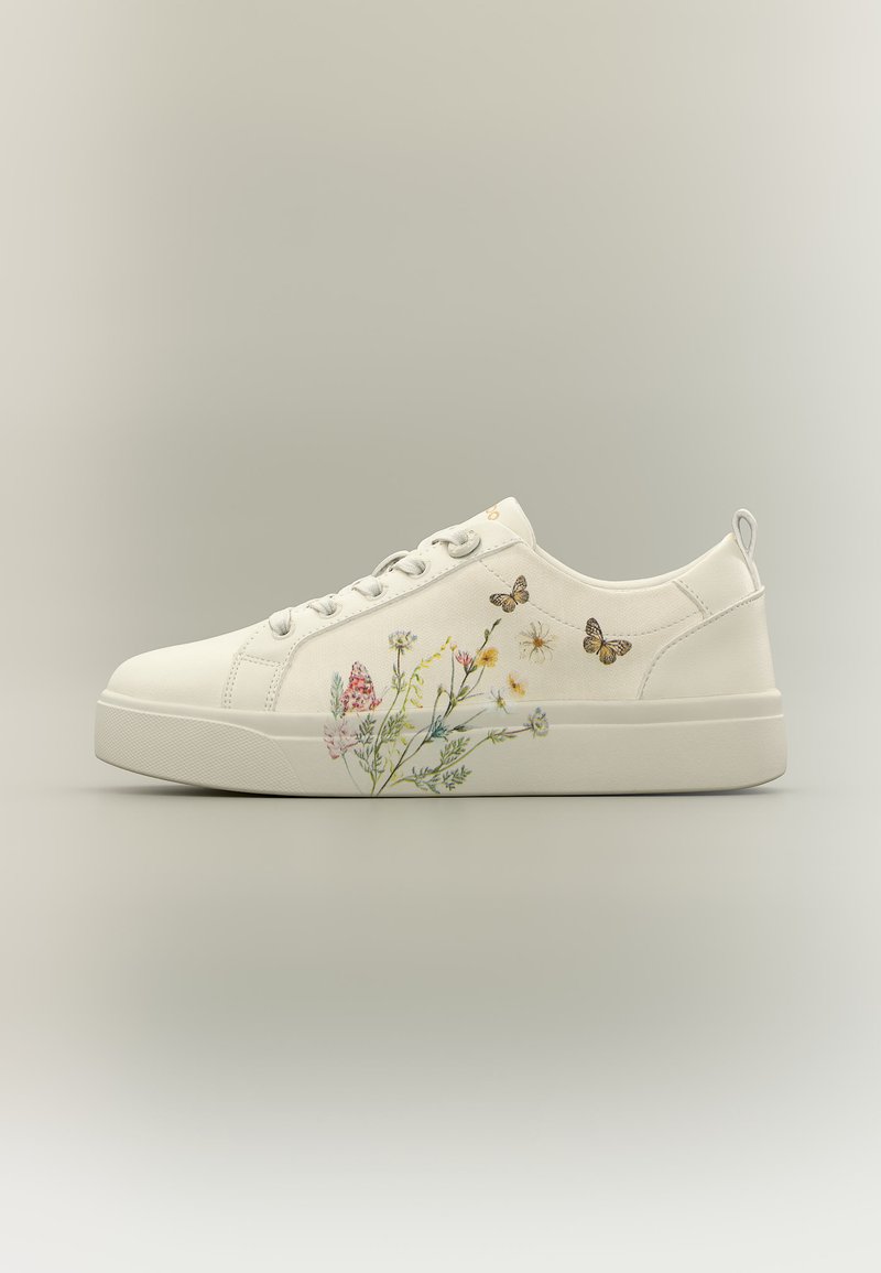 Zapatilla blanca de corte bajo con cordones en la parte delantera, que presenta detallados diseños de flores y mariposas en el lateral sobre un fondo neutro.