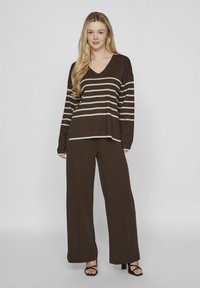 Haut à manches longues rayé marron avec un décolleté en V et un pantalon large assorti. Matière douce, coupe décontractée, avec un motif subtil de rayures beiges.