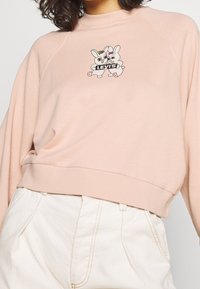 Ljusrosa sweatshirt med en avslappnad passform, ribbade ärmslut och en lekfull tecknad grafik med två kaniner på bröstet.