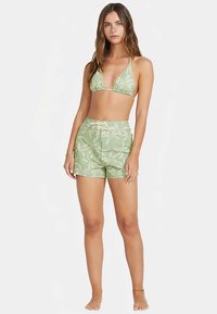 Top de biquíni verde com alças finas e calções de cintura alta combinando, ambos com padrão de folhas. Tecido macio com textura leve.