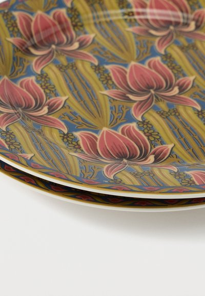 Assiettes en céramique empilées avec des motifs floraux complexes en tons rouges, bleus et dorés sur une surface blanche.