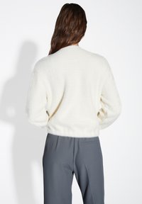 Maglione a crema strutturato con collo rotondo, maniche lunghe e un taglio corto, abbinato a pantaloni grigi con una tasca laterale.