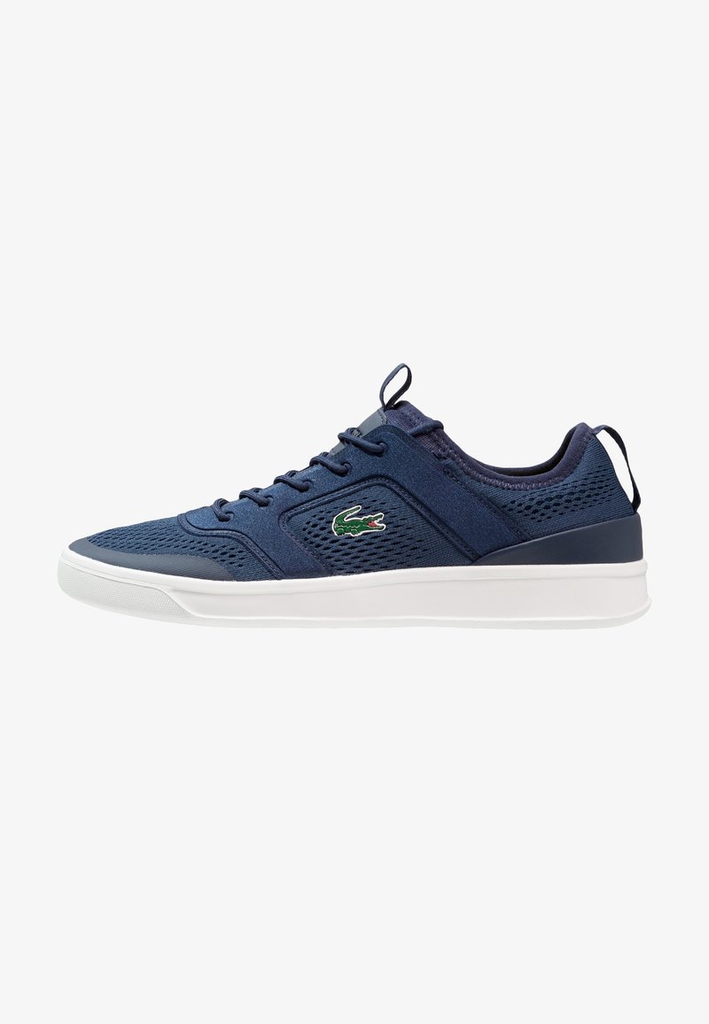 Baskets bleu marine avec dessus en mesh et tissu, semelle blanche, design à lacets, languette et talon avec languette de tirage, et logo crocodile vert sur le côté.