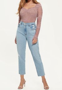Langärmliger mauvefarbener Spitzenbody kombiniert mit hellblauen, hochgeschnittenen Jeans, die abgenutzte Details und rohe, ausgefranste Säume aufweisen.